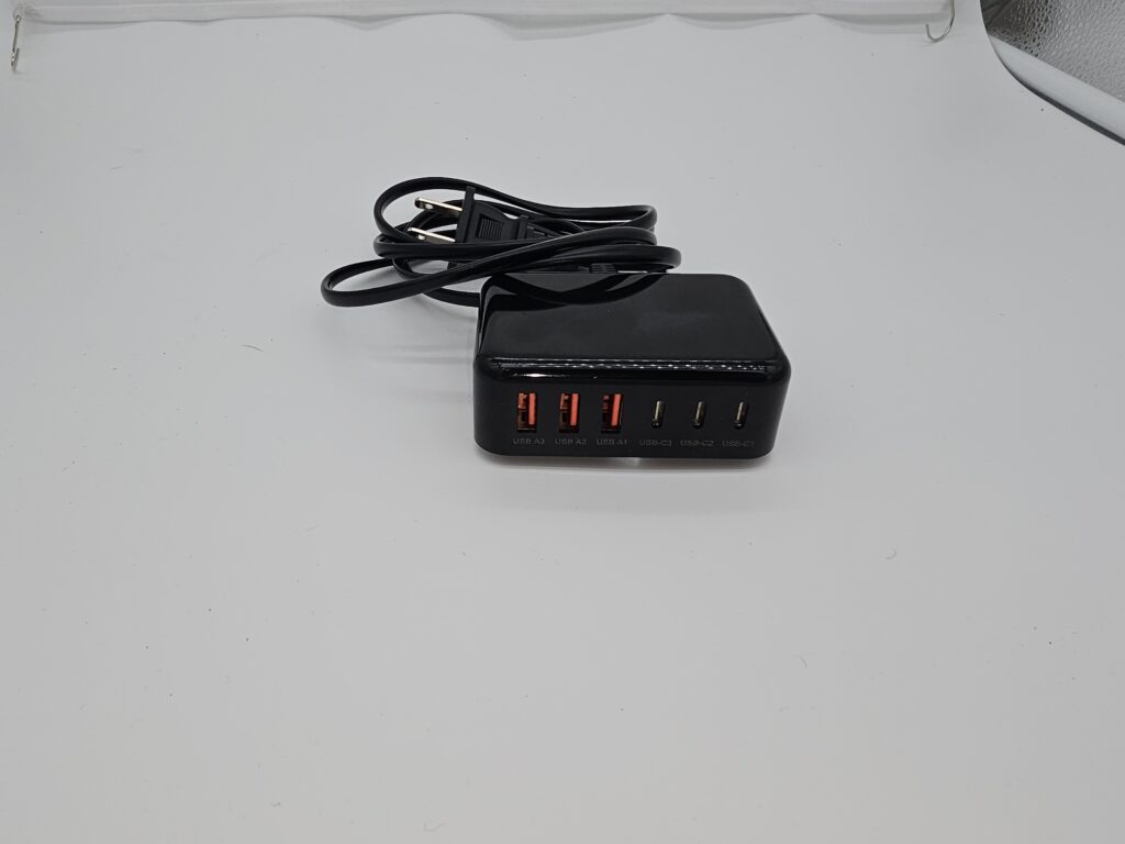Black cube-style 6-port USB charging adapter with 3 USB-C and 3 USB-A ports, labeled ‘100 W’, with attached 5 ft AC extension cord.