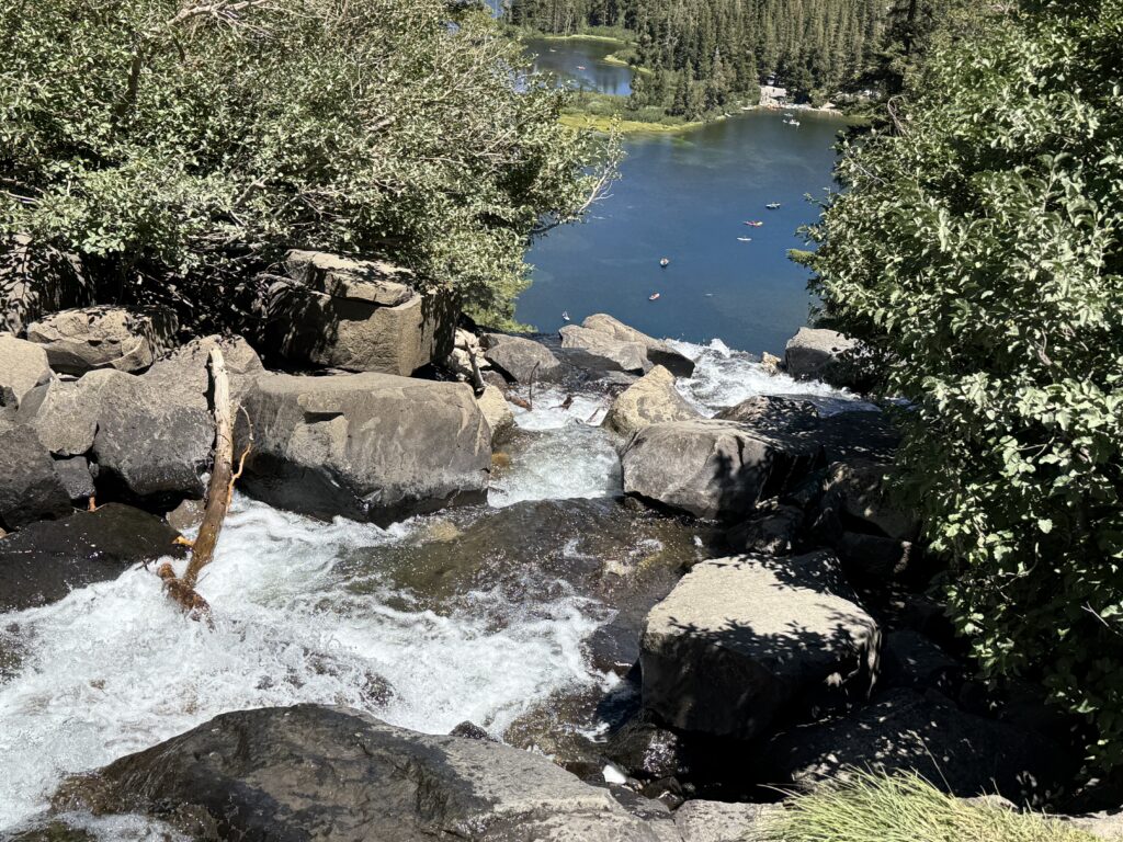 View from Twin Falls Overlook in Mammoth Lakes, California, looking down at Twin Lakes with kayakers paddling across the calm blue water surrounded by pine forests and mountain peaks.