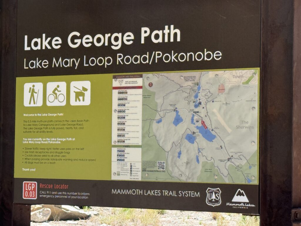 Trail sign marking the start of the Lake George Path in Mammoth Lakes, California, surrounded by evergreens and mountain scenery on a clear day.